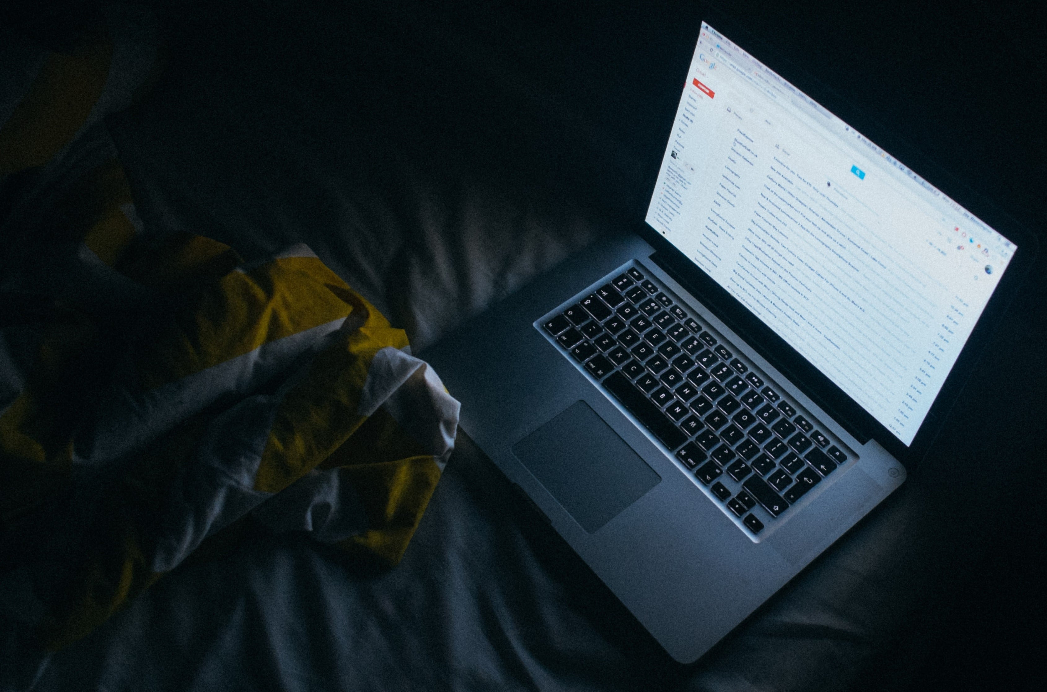 laptop on a bed in the evening emitting harmful bright light that blue light blocking glasses can be used for protection