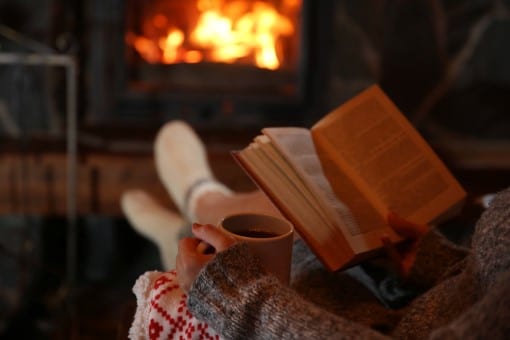 Person relaxing before bed with a cup of tea by the fireplace as described on the sleep checklist