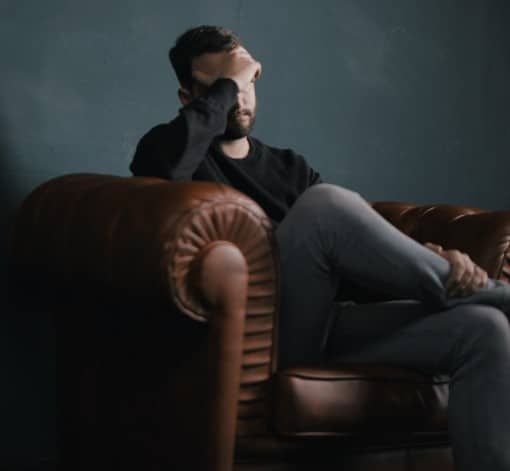 Man sitting on the couch whose nausea is keeping him from falling asleep