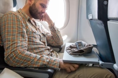  Man sitting on plane who can’t sleep during holidays because of jetlag