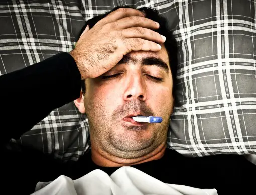 sick man awake in bed with thermometer in mouth