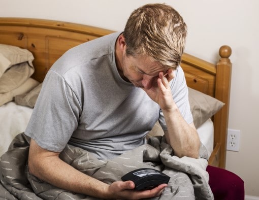 man frustrated from waking up too much to go to bathroom looking at clock