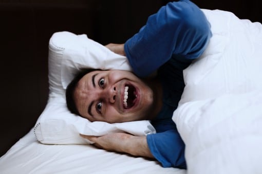 frustrated man awake in bed who wants the best fan for white noise 