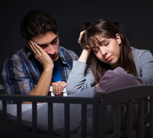 upset couple sitting by crib because barking dog wakes up the baby