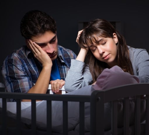 When a barking dog wakes up the baby, it can ruin your night upset couple sitting by crib because barking dog wakes up the baby