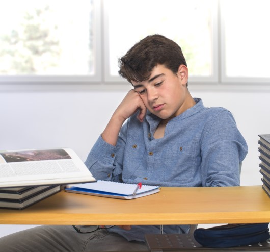 photo of tired teen sitting at class desk 