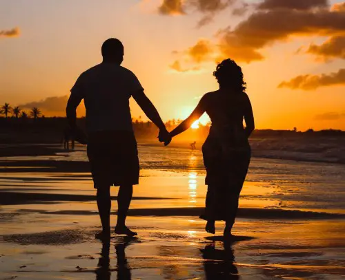 photo showing couple walking on beach in the evening