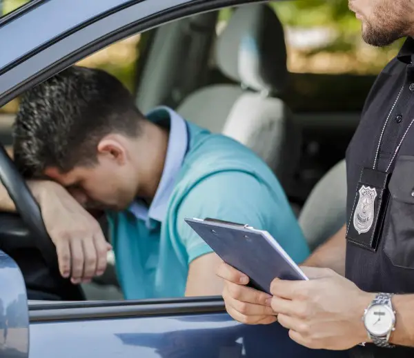 photo of sleep-deprived teen sitting in car getting a ticket from a police officer