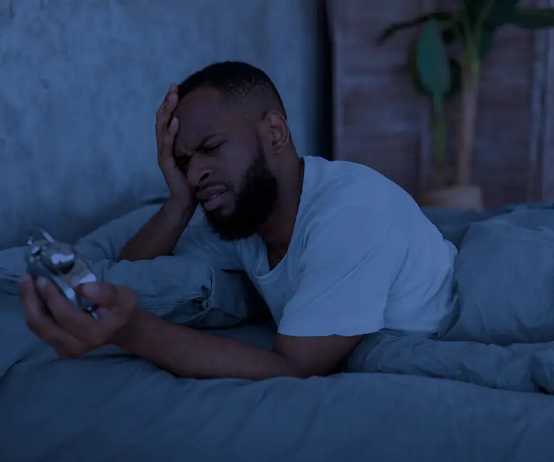 adult male sleepless in bed looking at clock after an argument